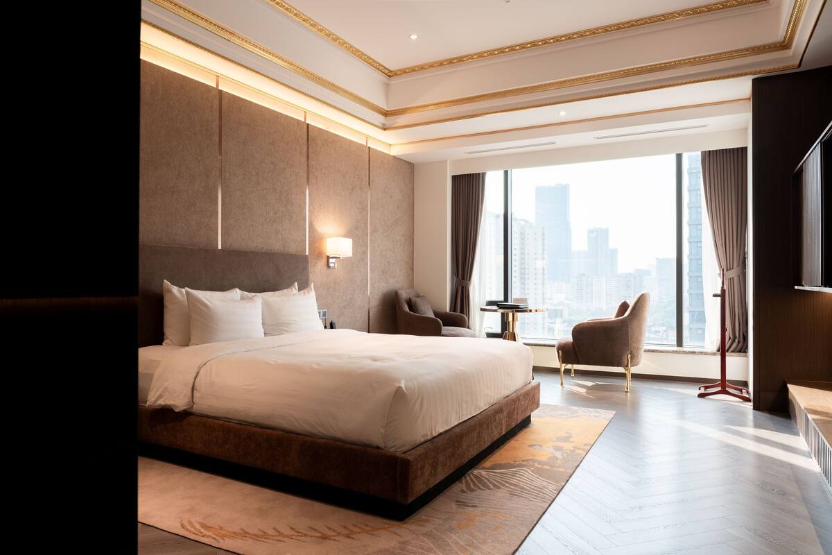 Een moderne hotelkamer met een groot bed, een zithoek en uitzicht over de stad.