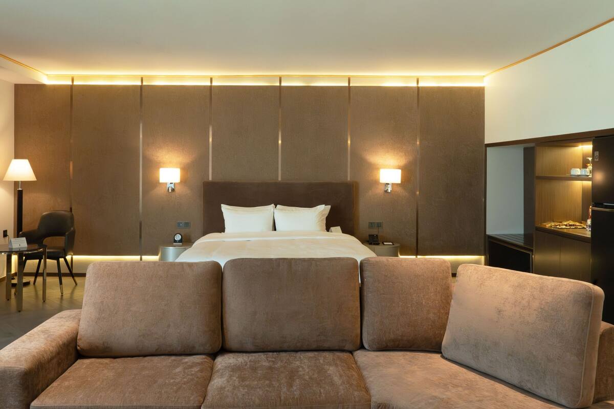 Een hotelkamer met een bed, twee bedlampjes, een klein tafeltje met een stoel en een bank.
