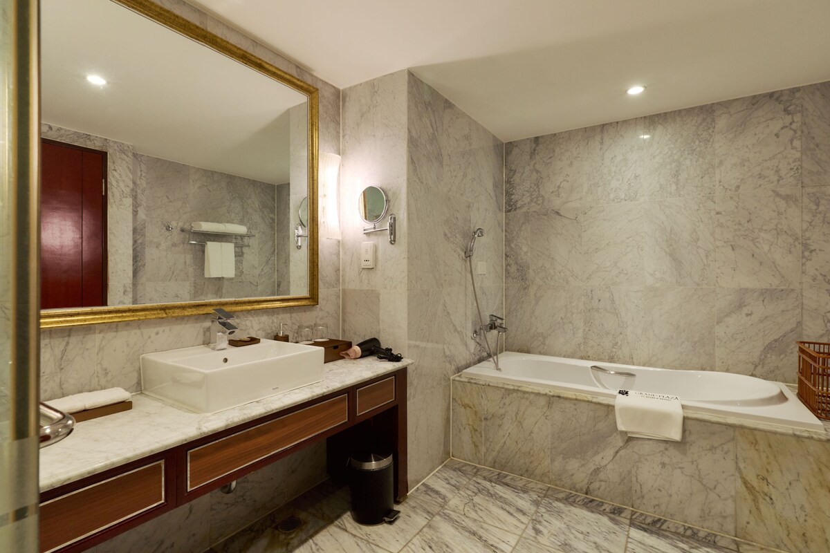 Une salle de bain avec un mur en marbre, un grand miroir, un lavabo, un meuble-lavabo et une baignoire.