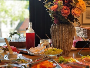 A buffet table with various food items, a decorative vase with flowers, and a bottle of red beverage.