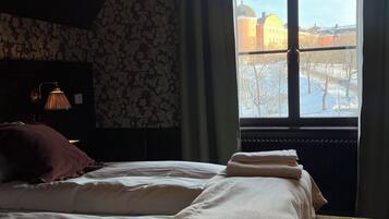 Un dormitorio con dos camas, un radiador, una lámpara y una ventana con vistas a edificios.