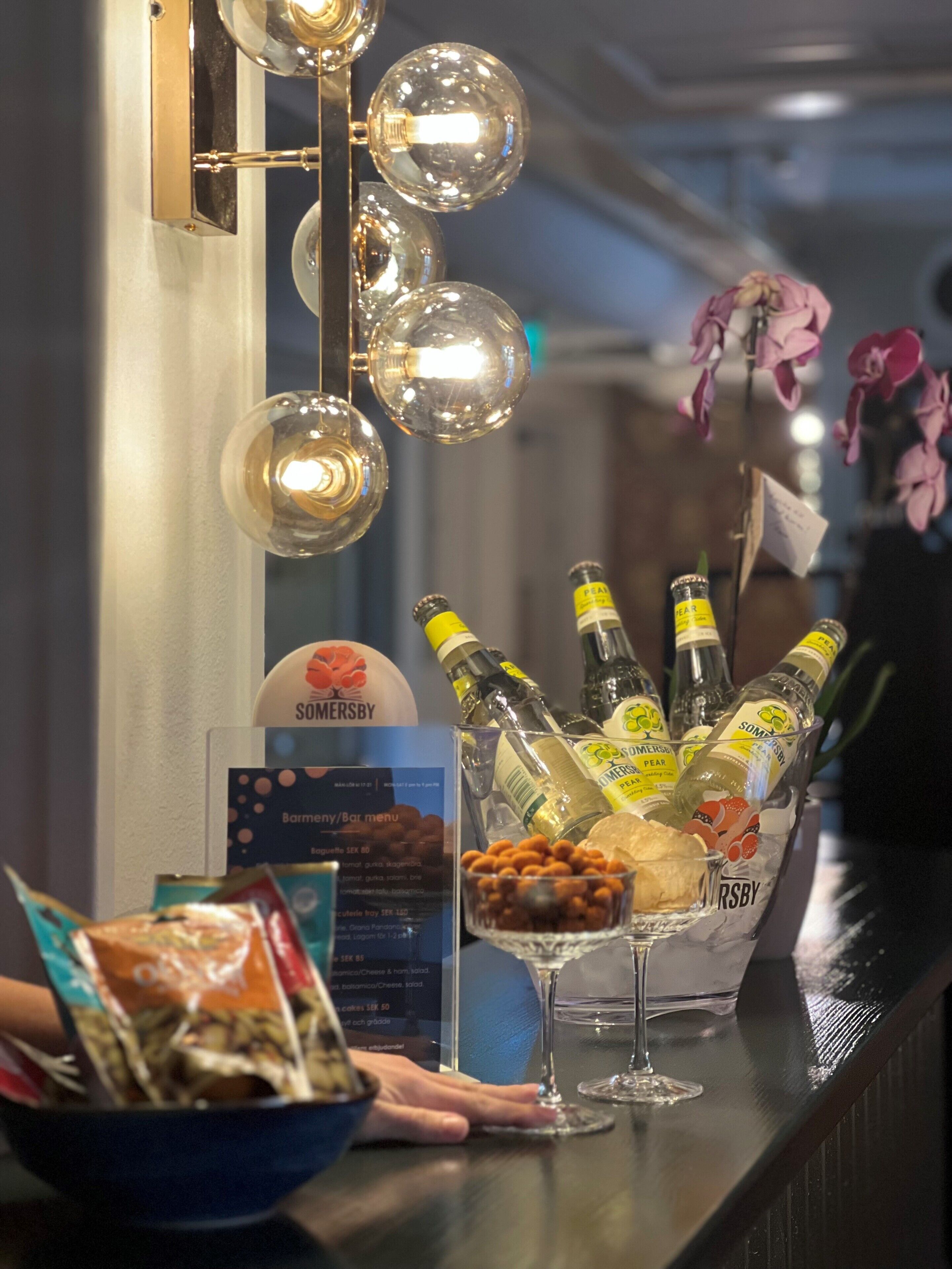 A bar area with bottles of SOMERSBY Pear, a bowl of nuts, and a menu board.