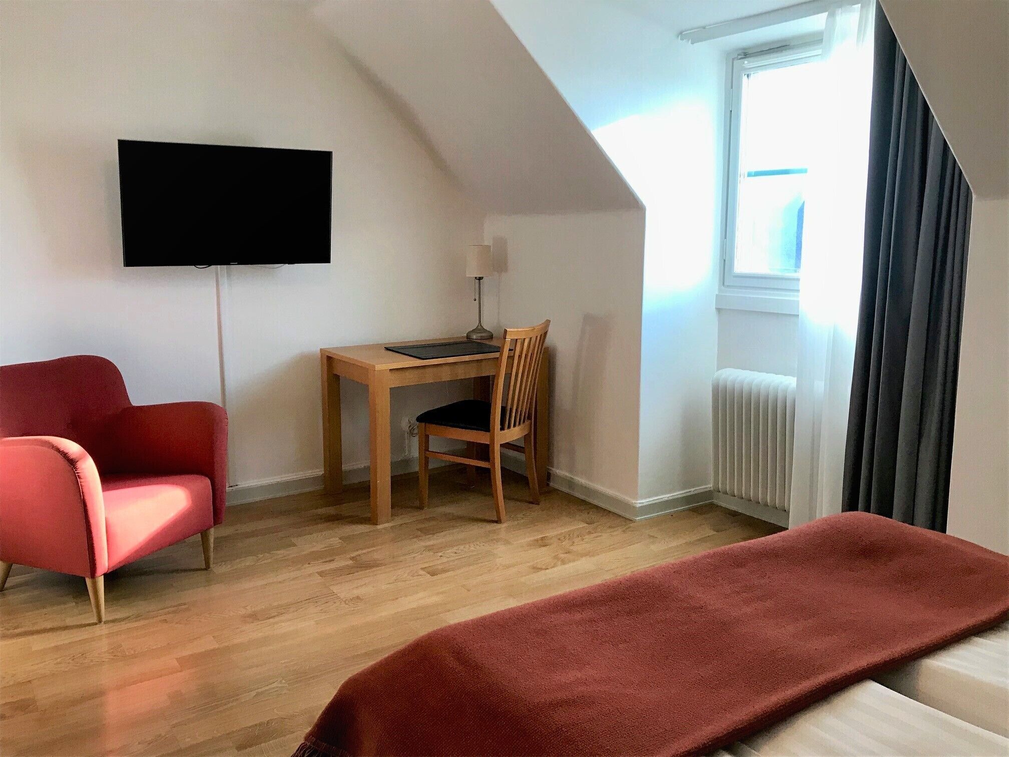 A room with a desk, chair, TV, and a window with curtains.