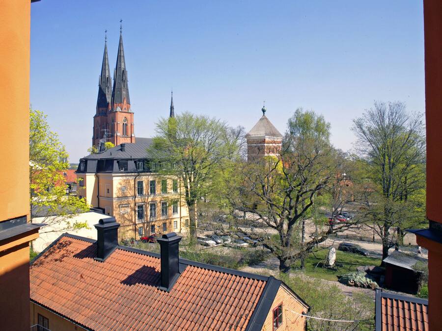 A view of a building with a red-tiled roof, a church with a tall spire, and a domed structure in the background.