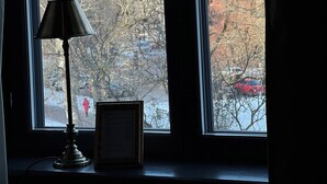 Una ventana con vistas a un edificio, una lámpara y un objeto enmarcado en el alféizar.