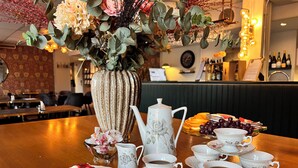 Una mesa servida con tazas de té, platitos, una tetera y una bandeja de pasteles.