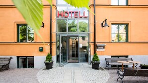 Entrada de un hotel con puerta de cristal, asientos al aire libre y un cartel que indica que es el 'Academy Hotel'.