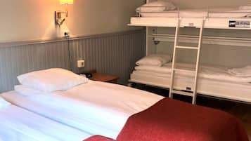 Een hotelkamer met twee bedden, waarvan één met een rode deken en de ander met witte lakens. Er is een wandlamp en een stapelbed met witte lakens.