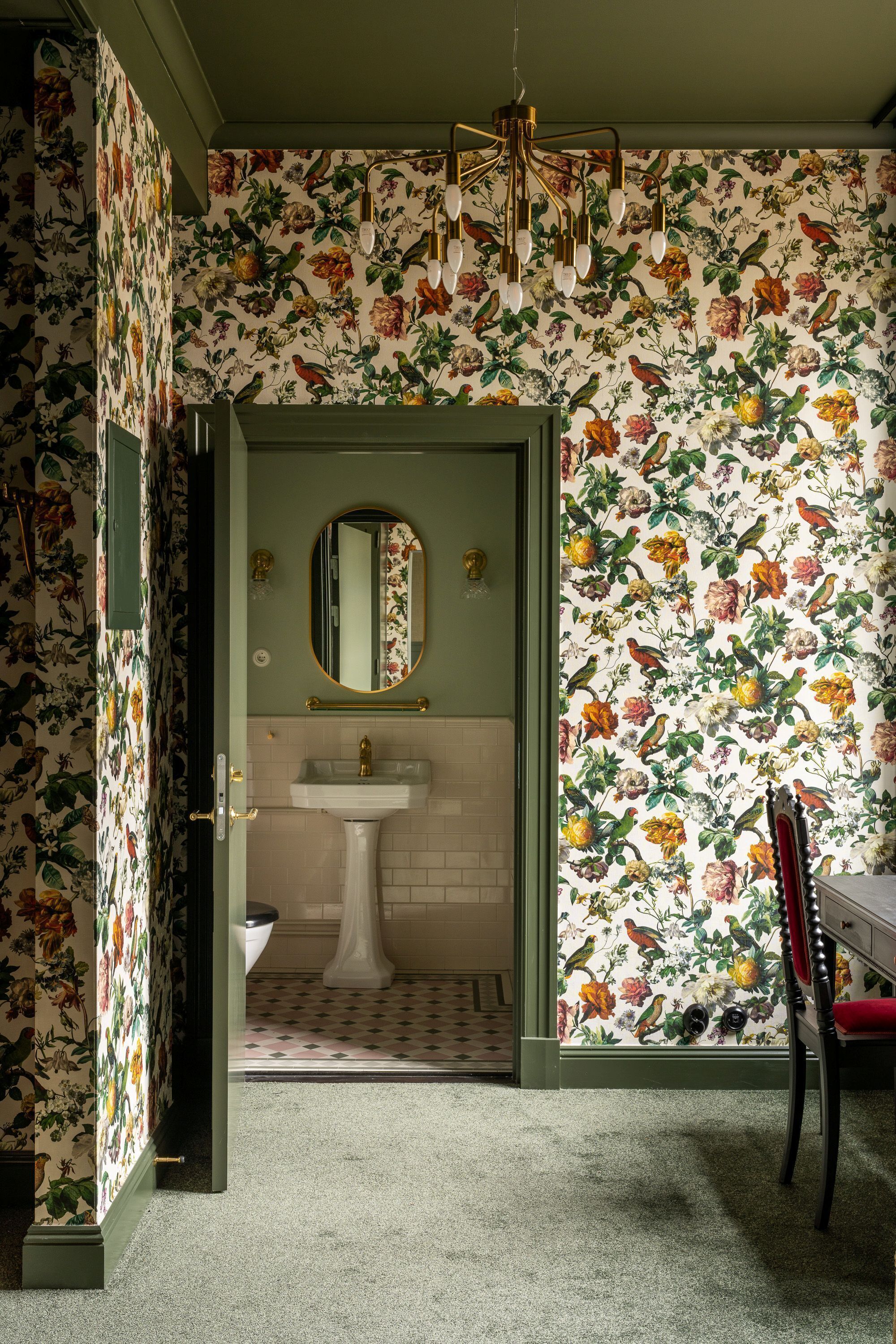 A bathroom with floral wallpaper, a pedestal sink, and a red chair.