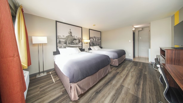 Een hotelkamer met twee bedden, een bureau, een stoel, een lamp en twee ingelijste foto's aan de muur.