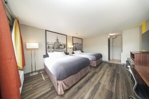 Habitación de hotel con dos camas, un escritorio, una silla, una lámpara y dos cuadros en la pared.