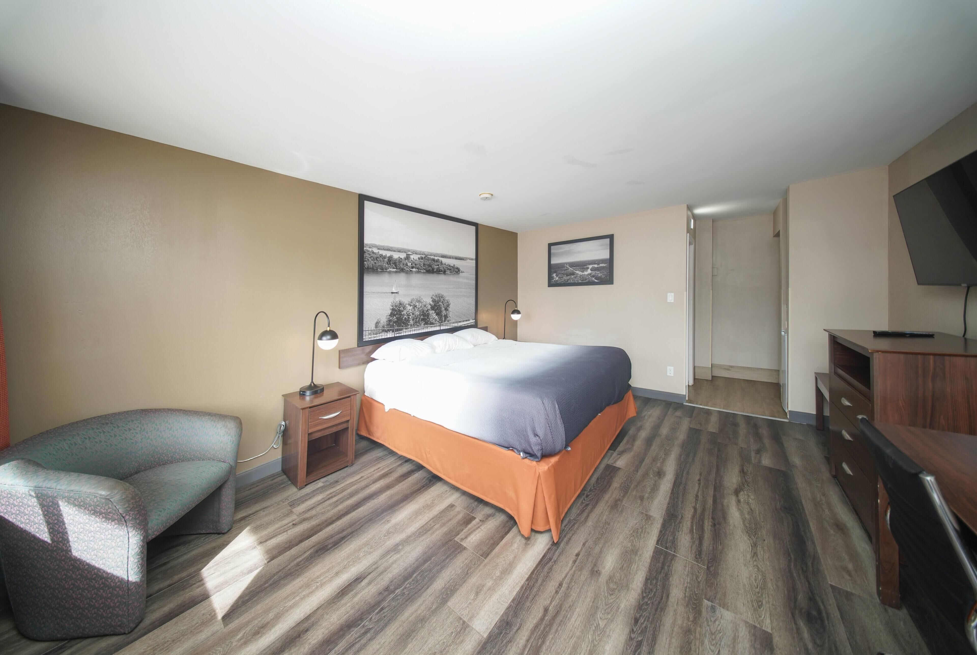 A hotel room with a bed, a chair, a desk, a TV, and a door leading to another room.