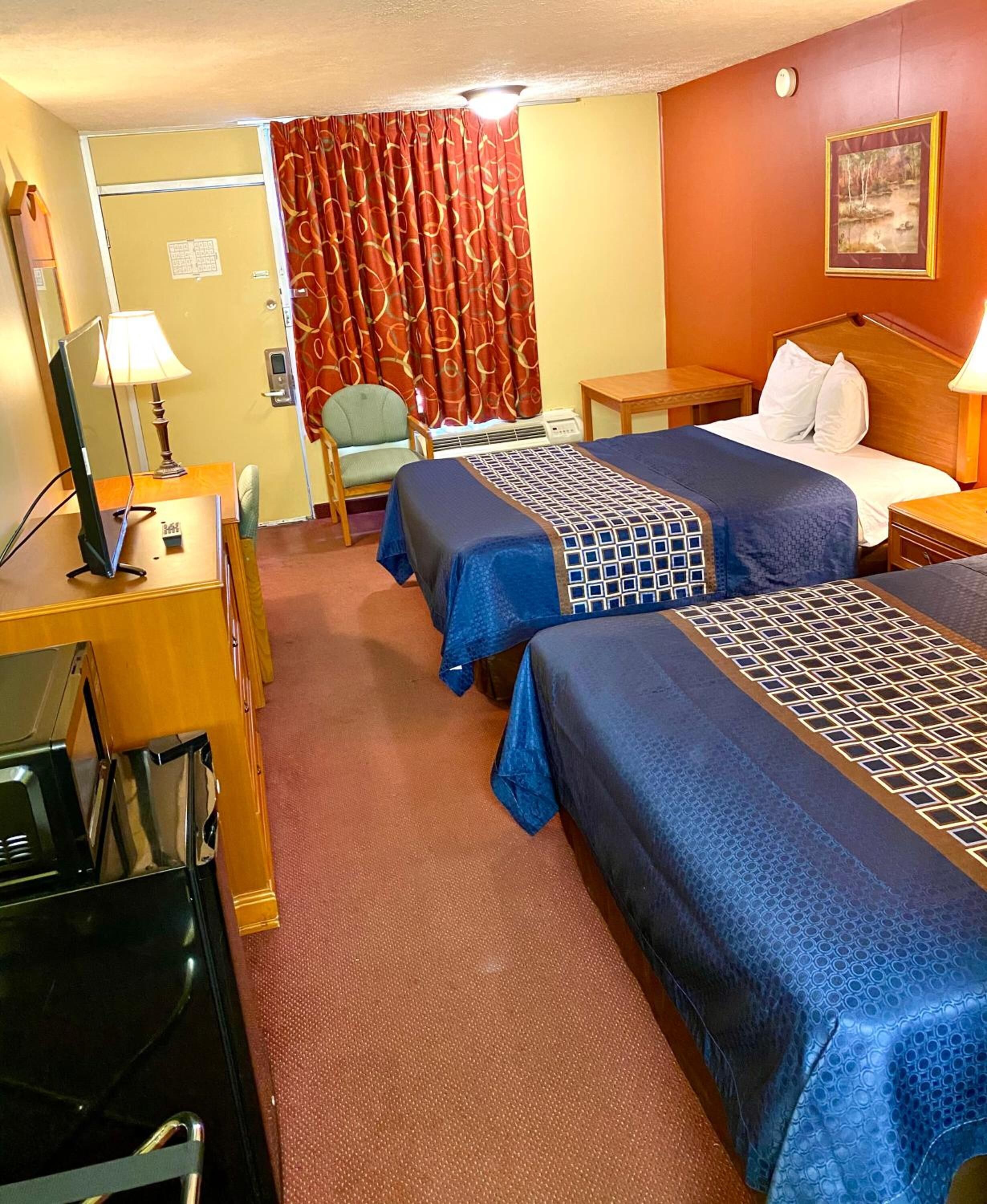 Une chambre d’hôtel avec deux lits, un bureau avec un ordinateur, une chaise et une fenêtre avec des rideaux.