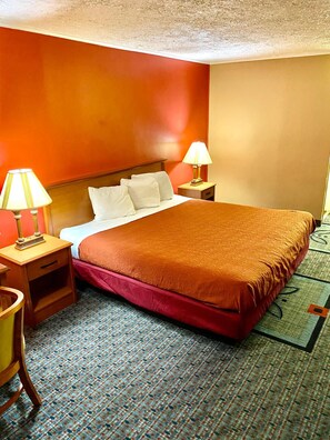 A hotel room with a large bed, two bedside tables with lamps, a wooden nightstand, and a patterned carpet.