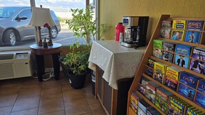 A cozy interior with a coffee machine, a small table with a lamp, a potted plant, and a display of books and board games. - Plaza Inn Springfield (Springfield)