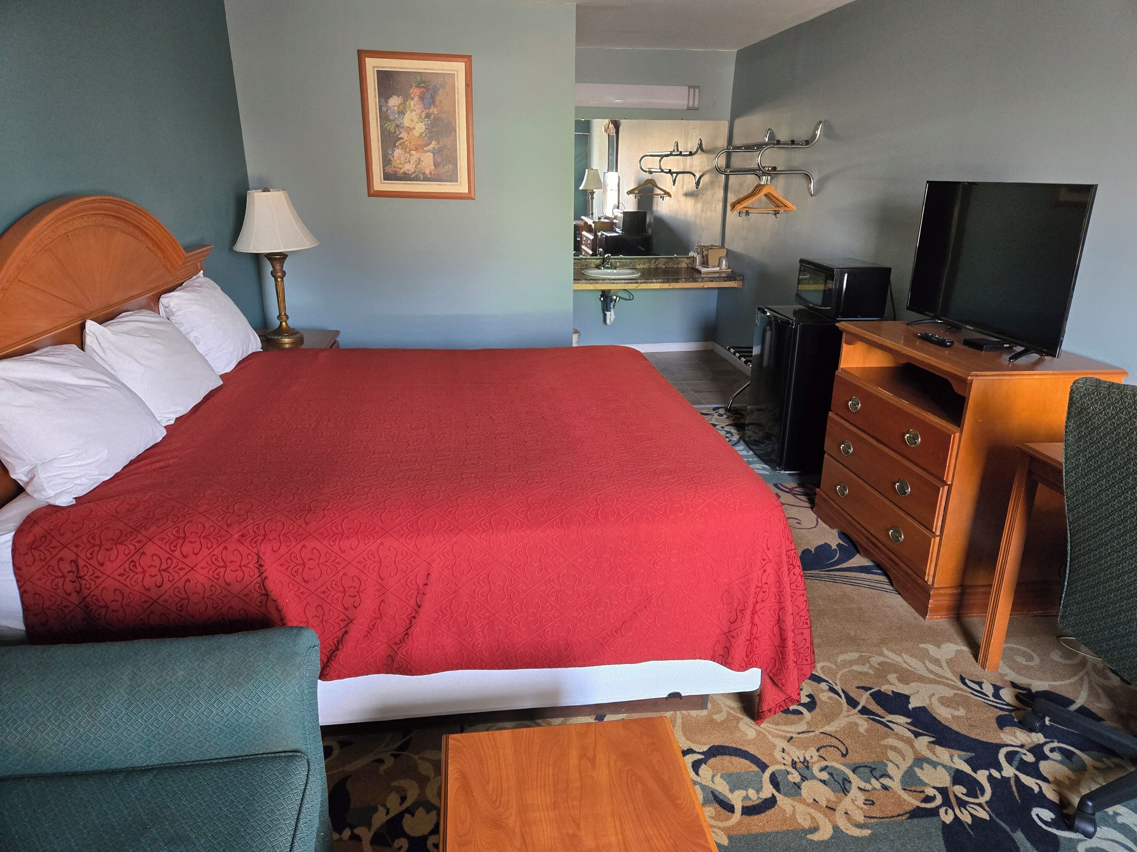 Een hotelkamer met een groot bed, een houten dressoir, een televisie en een bureau met een stoel.