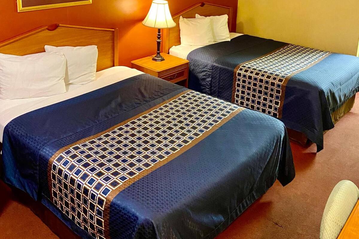 A hotel room with two beds, a nightstand with a lamp, and two framed pictures on the wall.