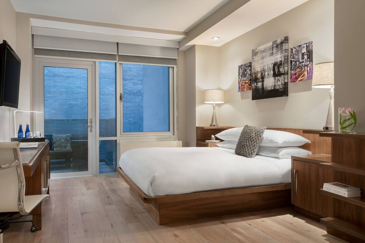 A modern hotel room with a large bed, a desk with a chair, a TV, and artwork on the walls.
