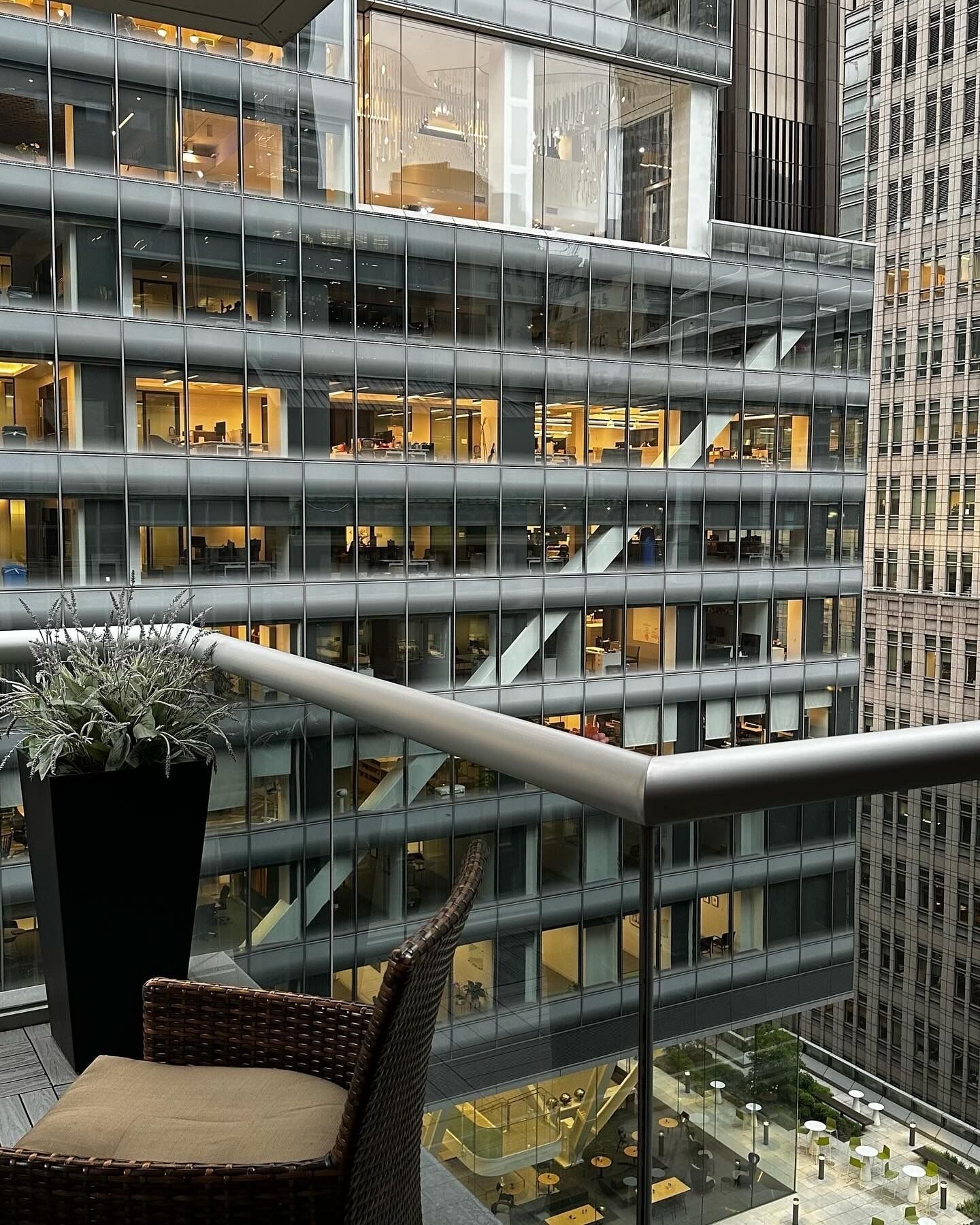 Ein modernes Gebäude mit Glasfassade, einem Balkon mit Korbmöbeln und einem Blumentopf.