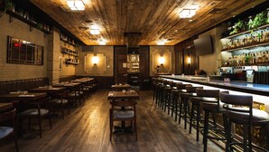 A restaurant with wooden floors and a bar area. There are tables and chairs arranged for dining. - The Gotham Hotel (New York)