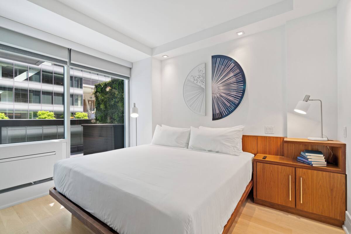 A modern bedroom with a large bed, a wooden nightstand, and a wall-mounted lamp.