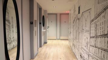 A hallway with a wooden floor, numbered doors, and a wall with architectural sketches.
