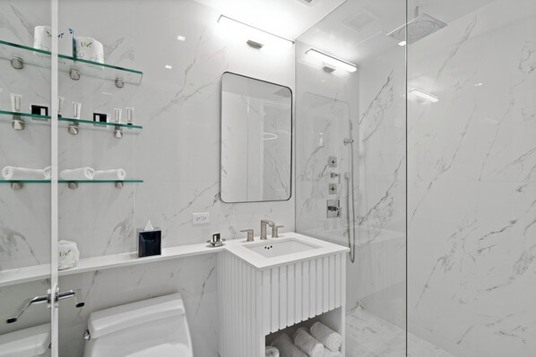 Une salle de bain moderne avec une douche à l’italienne en verre, un lavabo blanc avec un miroir et des murs en marbre.