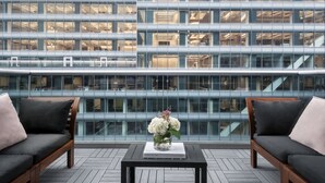 A modern building with a glass facade and a view of the interior. There is a black table with a vase of flowers in the foreground. - The Gotham Hotel (New York)