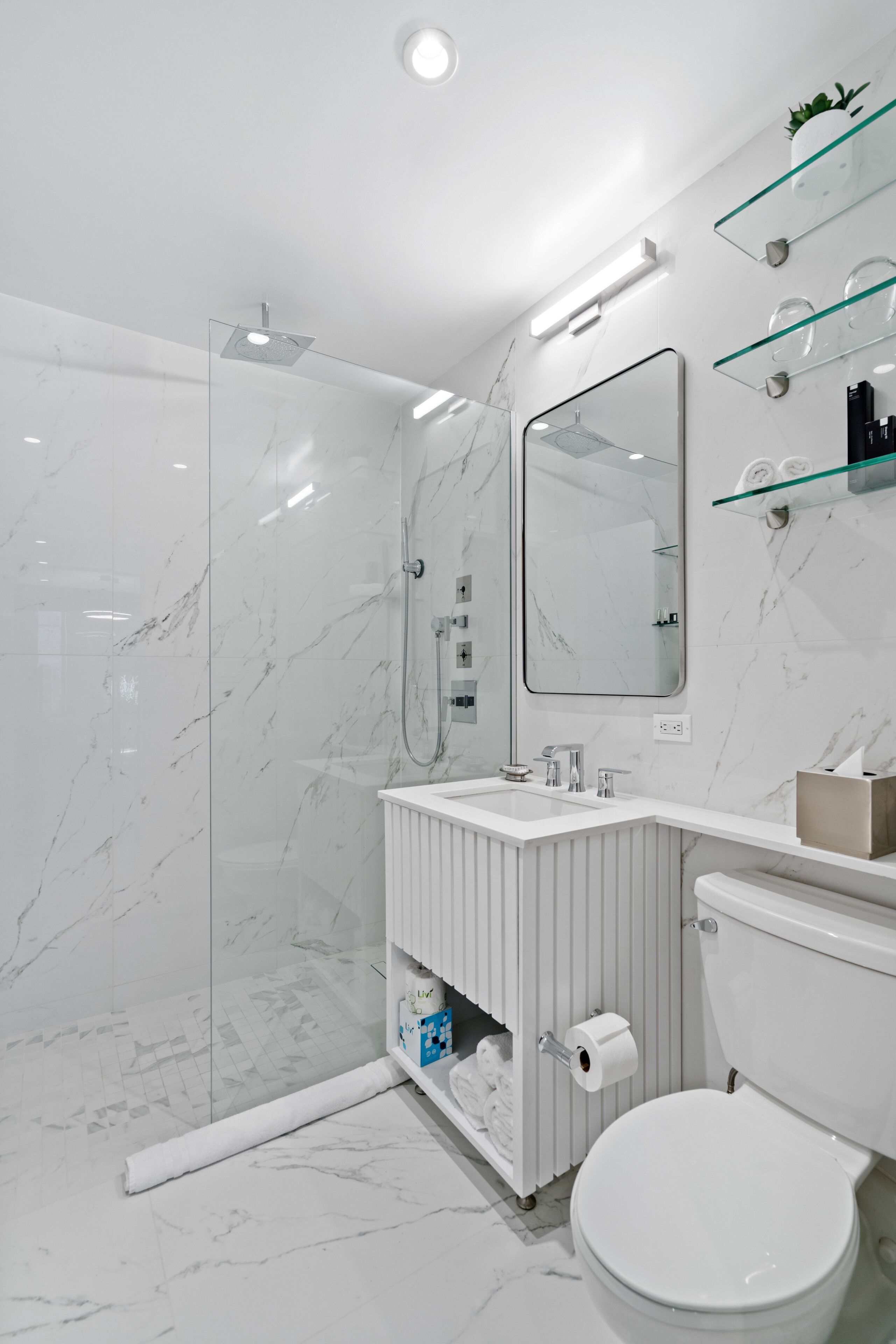 A modern bathroom with a glass shower enclosure, a white marble sink, and a toilet.