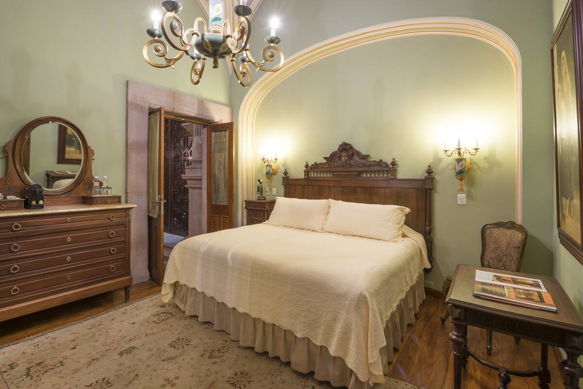 Une chambre à coucher avec un lit en bois, une commode, un miroir et un lustre.