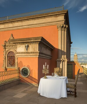 A terrace with a table set for dining, ornate architectural details, and a view of a distant tower. - Hotel Museo Palacio de San Agustin (San Luis Potosi)