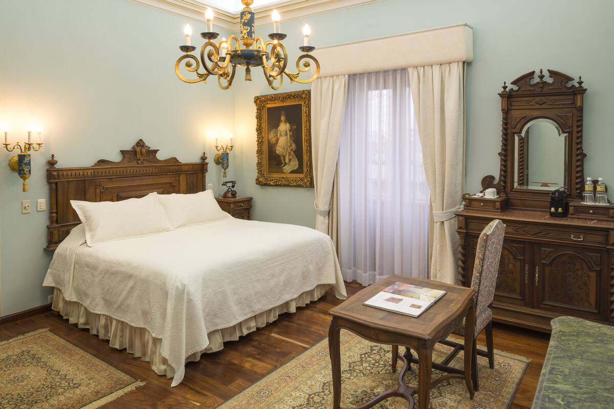 Une chambre à coucher avec un grand lit, une commode en bois, un lustre et un miroir.