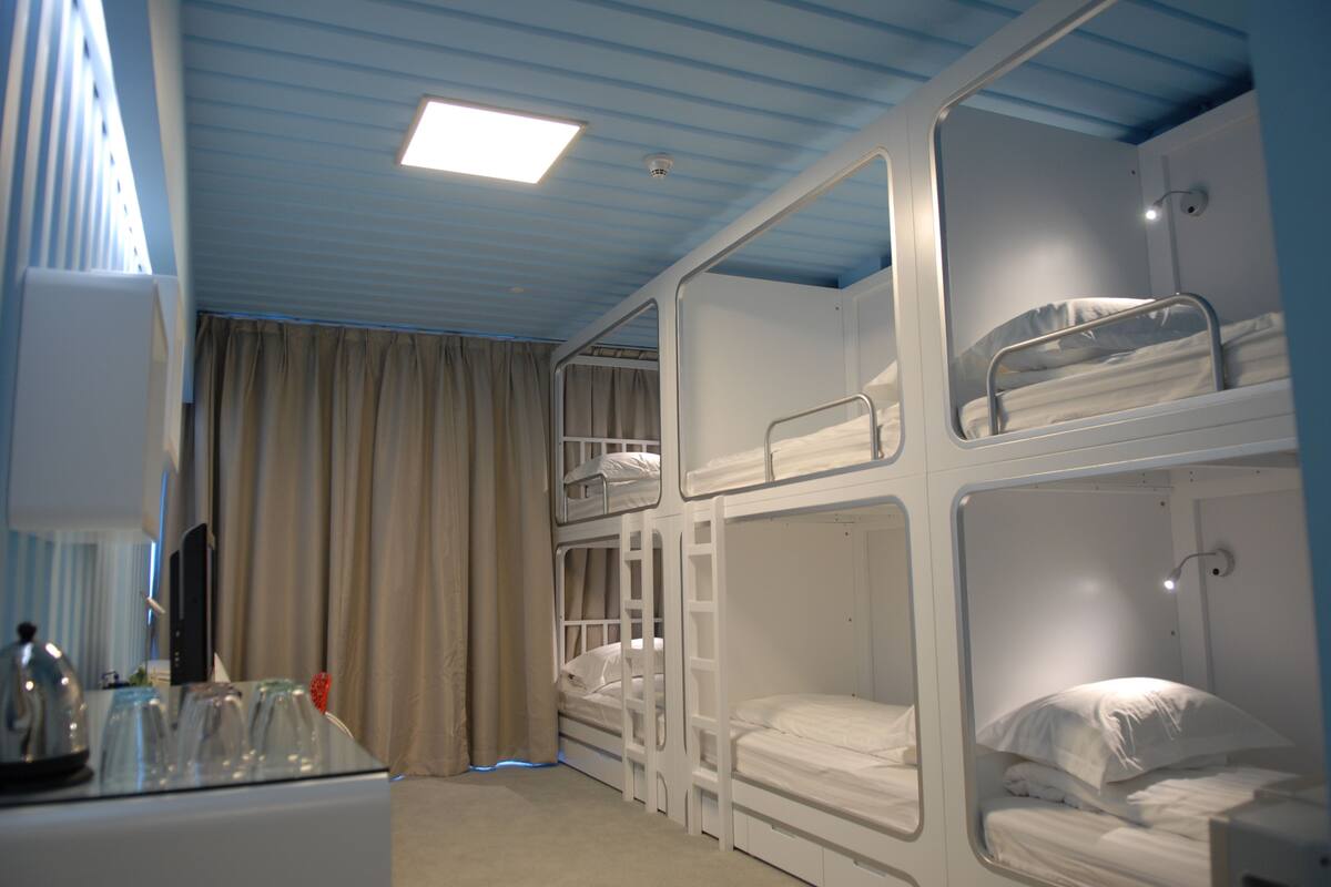 A hotel room with bunk beds, a desk with a kettle, and a window with curtains.