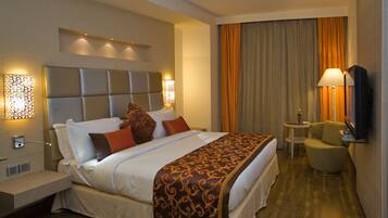 A hotel room with a large bed, bedside lamps, a small table with a chair, and a TV.