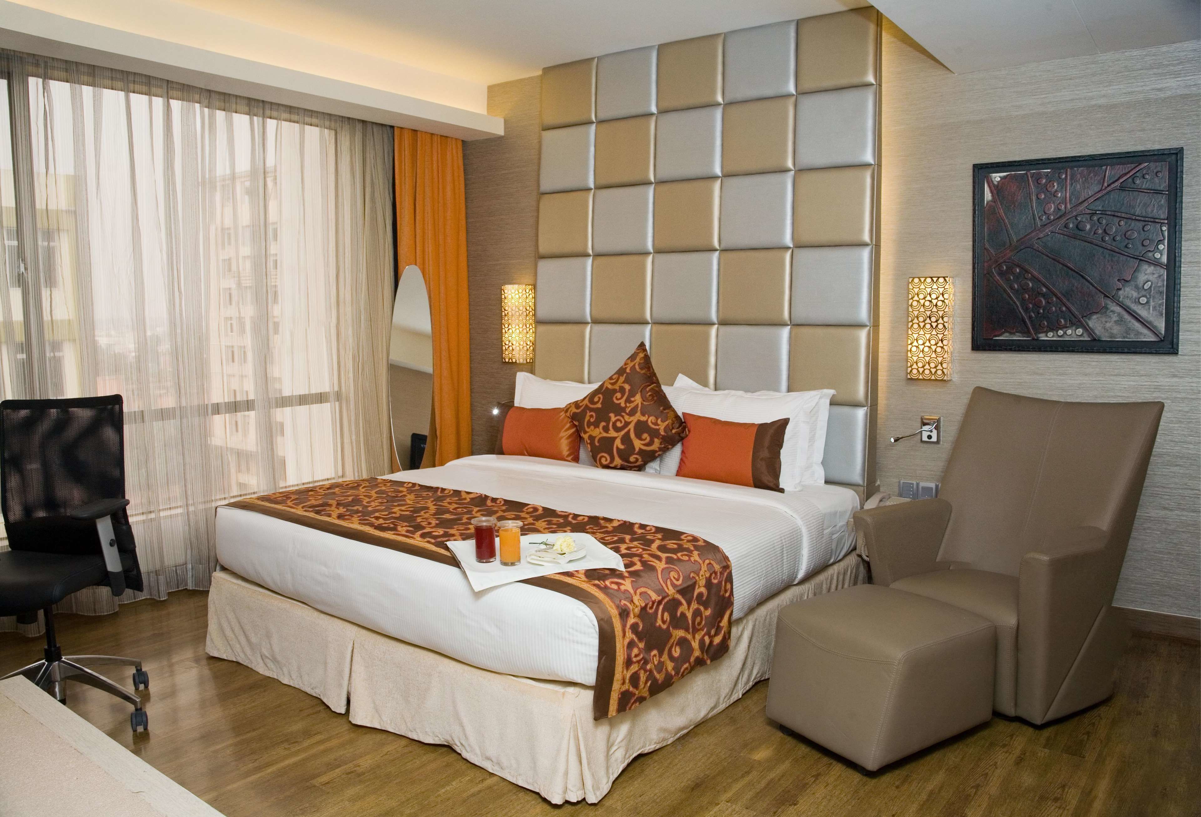 A hotel room with a large bed, a desk, a chair, and a view of the city through the window.