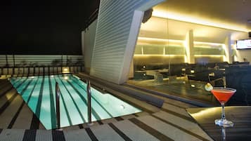 A pool area with a glass barrier, a bar area with a drink, and a view of the interior space.
