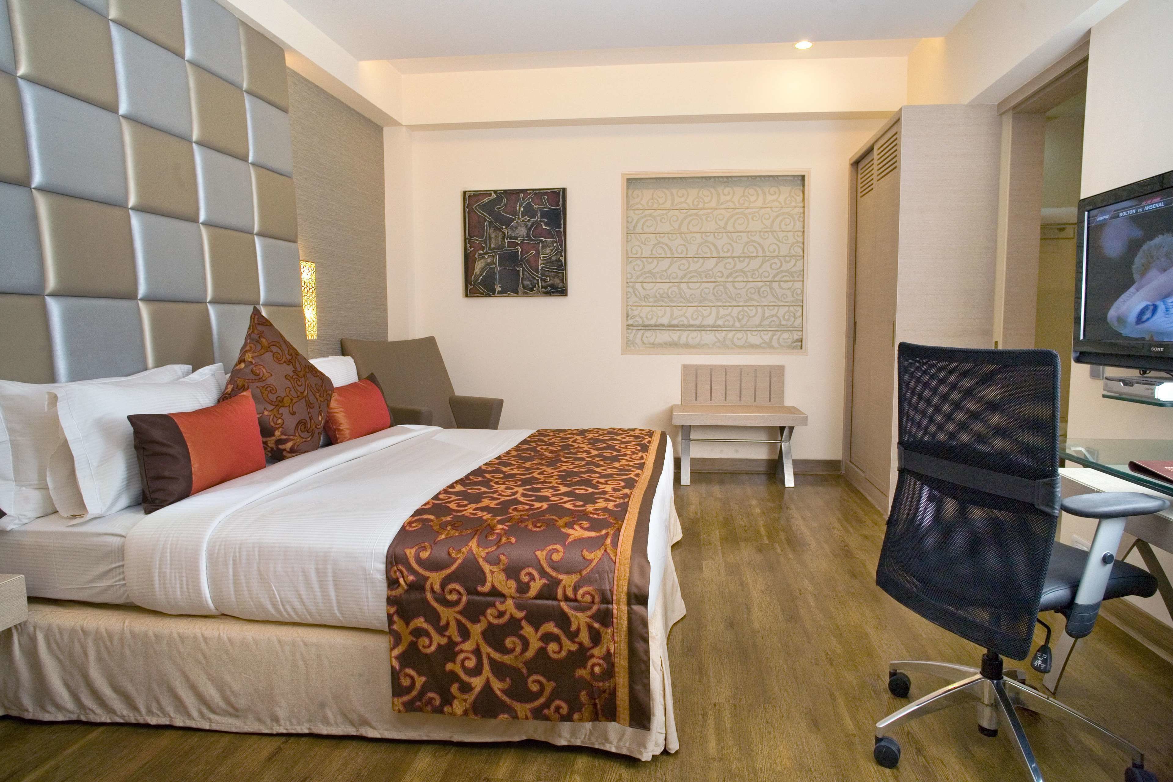 A hotel room with a bed, a desk, a chair, and a television.
