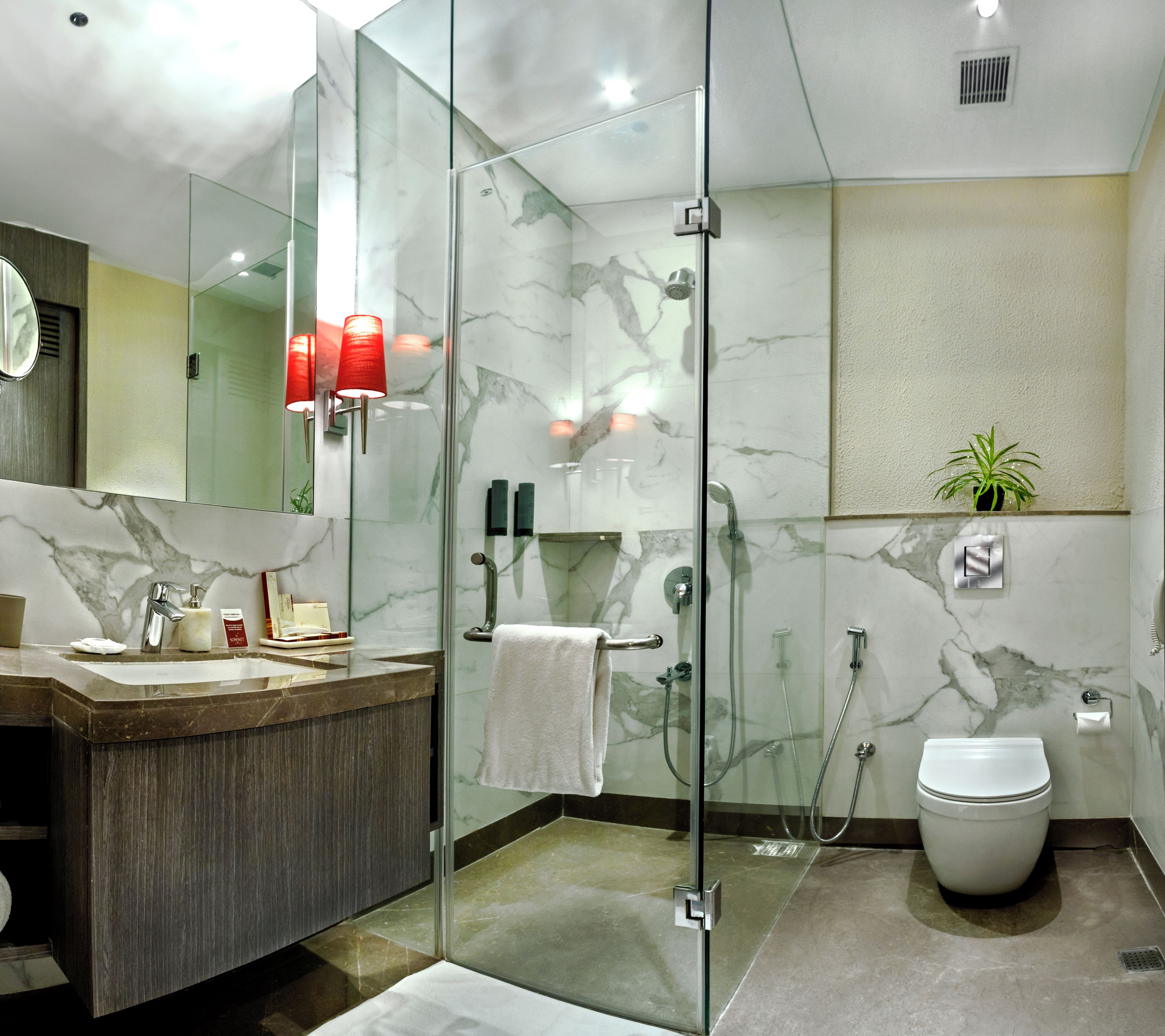 A modern bathroom with a glass-enclosed shower, a marble-tiled wall, a wooden vanity, and a toilet.