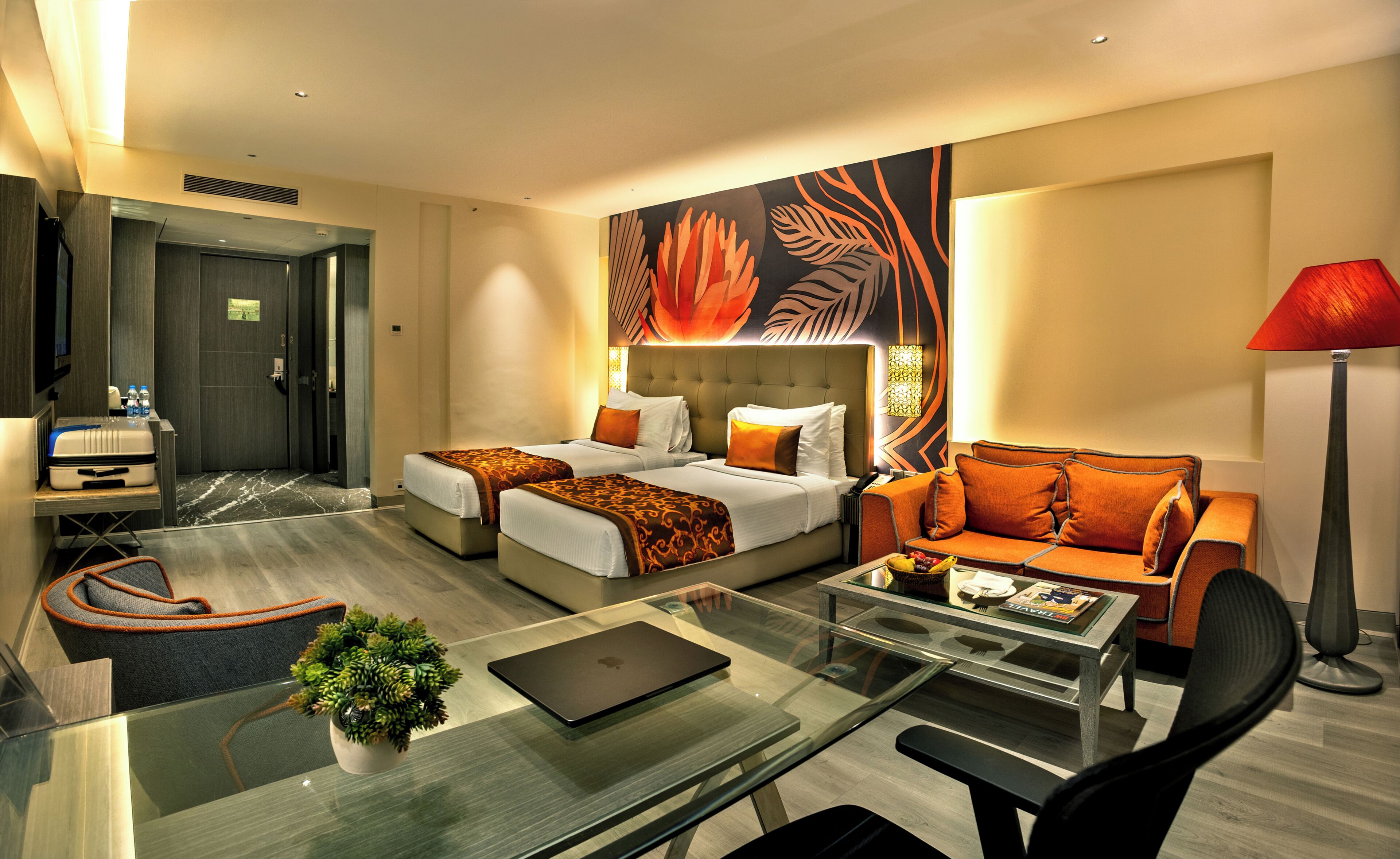 Hotelkamer met twee bedden, een glazen tafel, een bank, een rode lamp en een groot bloemenmural op de muur.