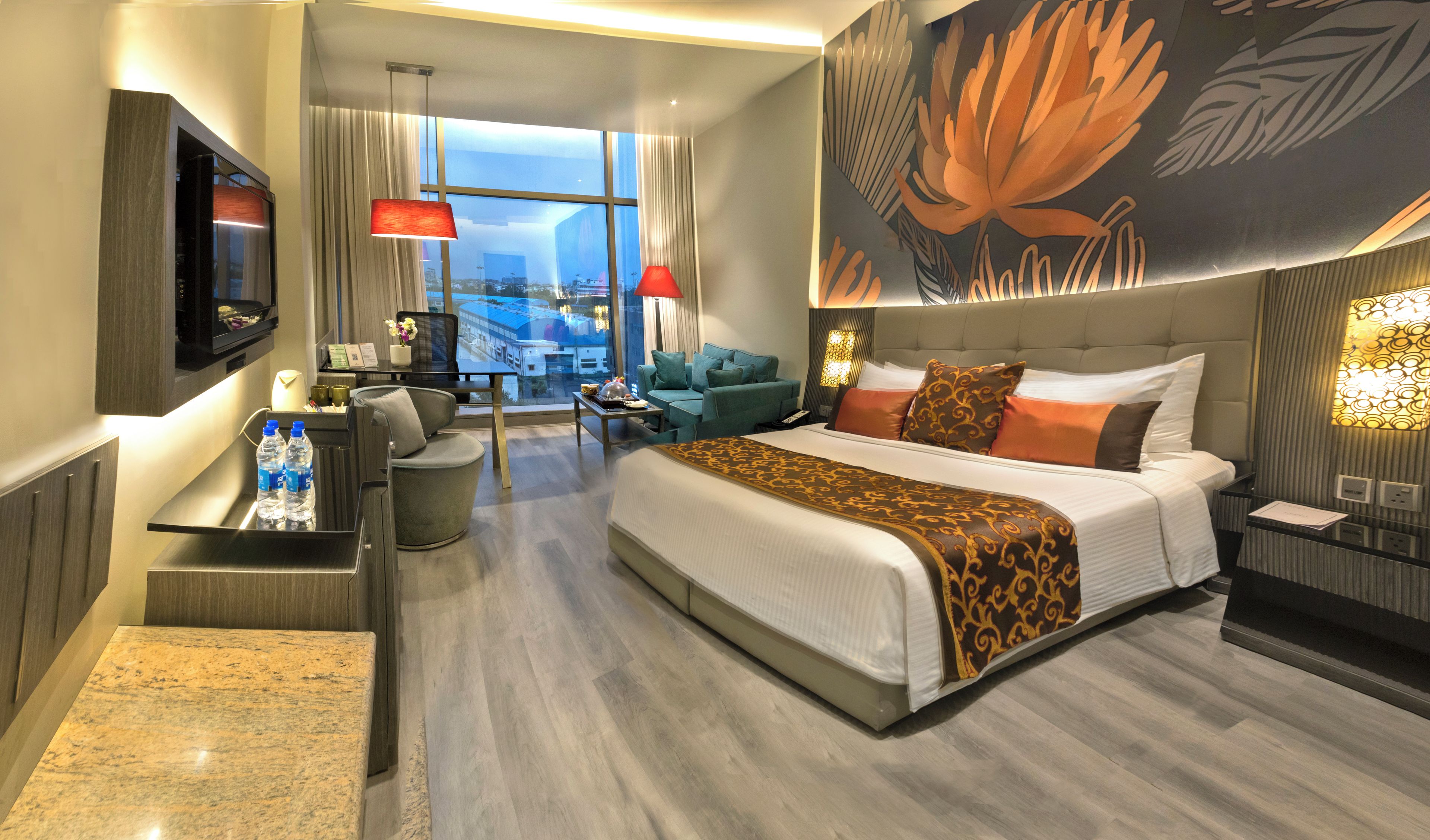 Habitación de hotel con cama, zona de estar, televisión y vista a la ciudad.