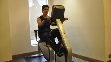 A person using a stationary bike in a room with a window, carpeted floor, and a plain wall.