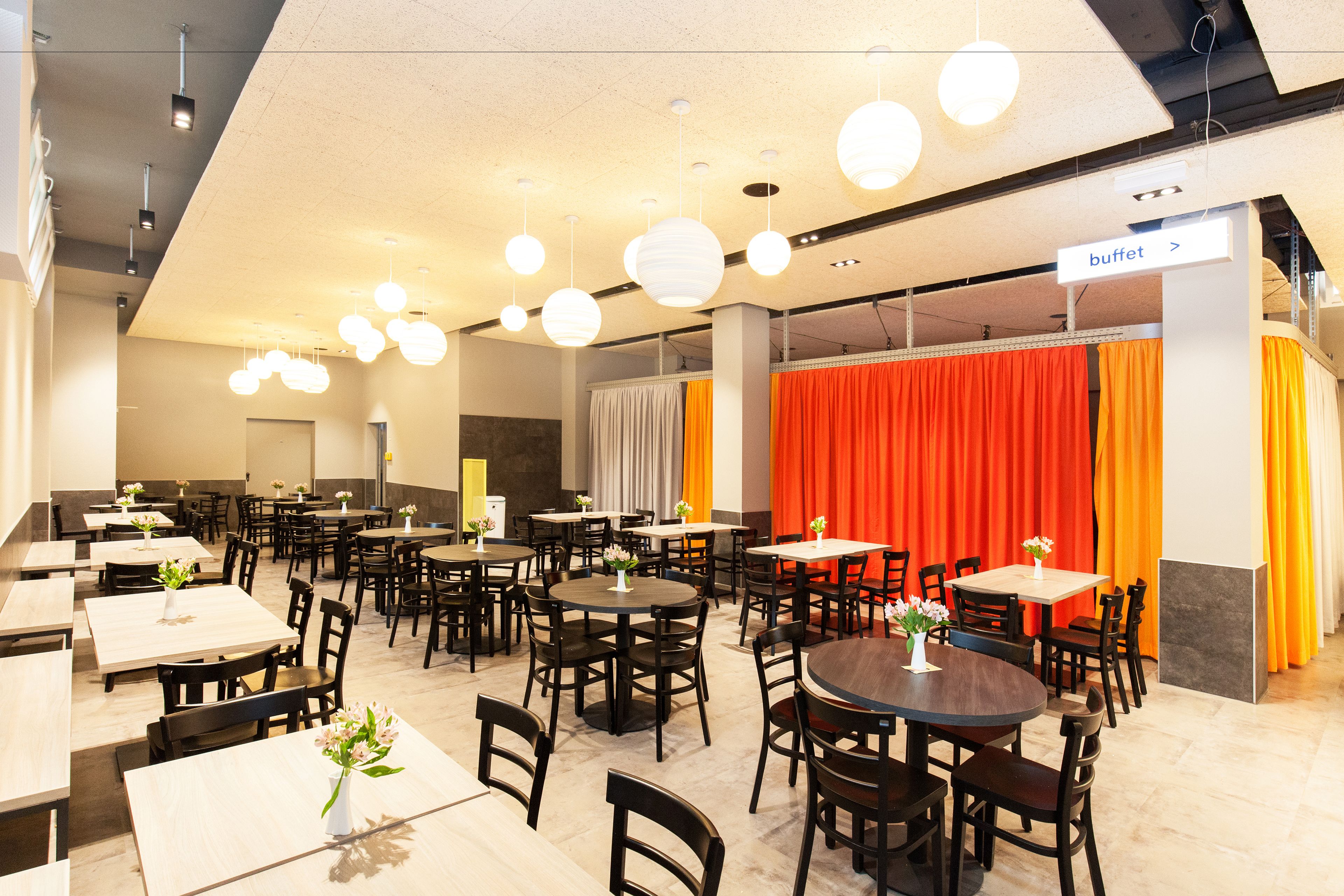 A spacious dining area with multiple tables and chairs, a buffet sign, and hanging spherical lights.