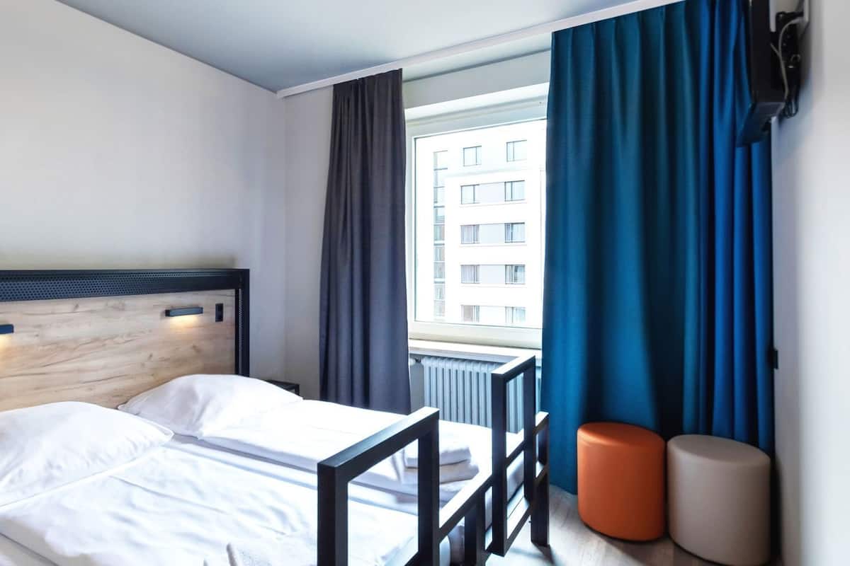 Ein Hotelzimmer mit einem Bett, einem Fenster mit Vorhängen, einem Heizkörper und einer Wand-Klimaanlage.