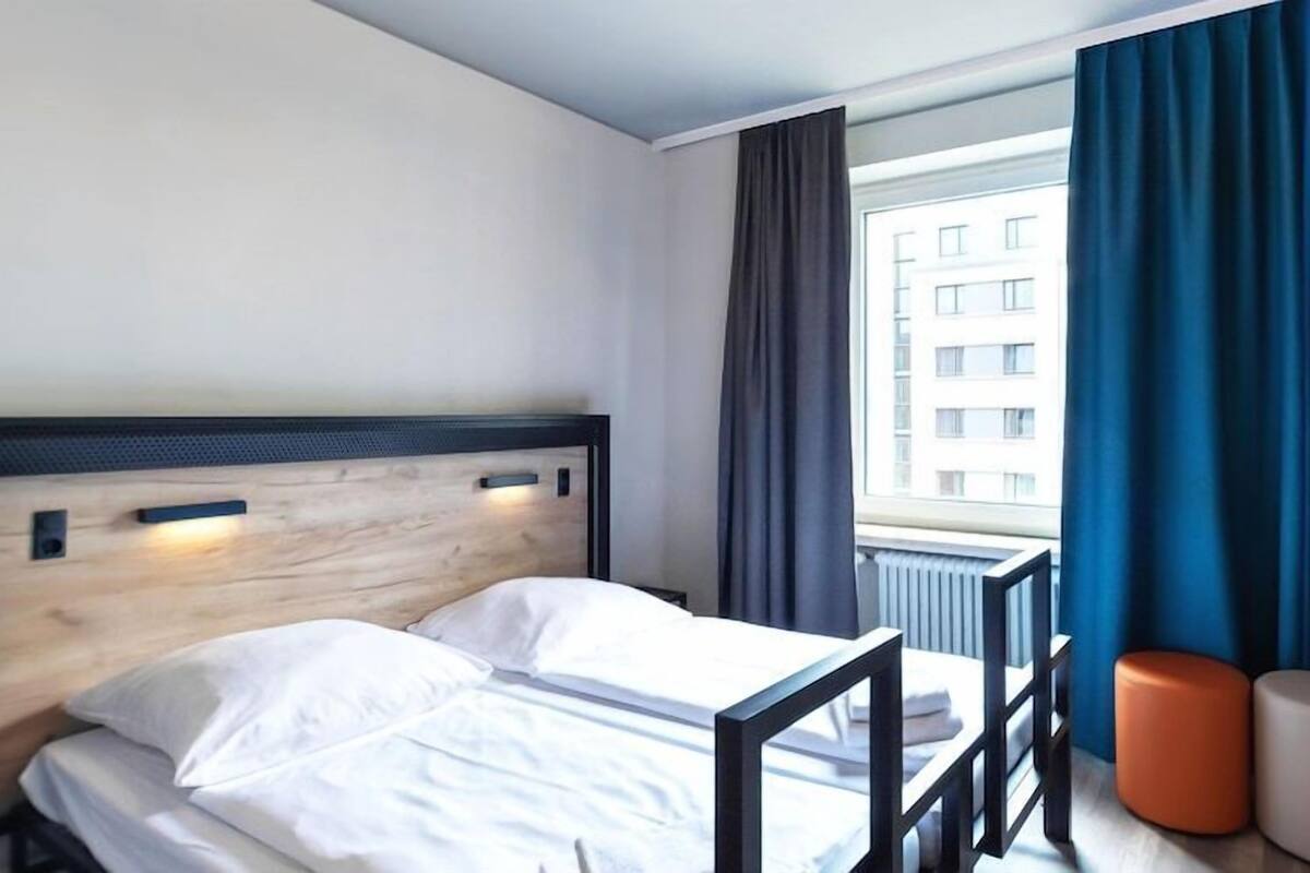 Ein Hotelzimmer mit Bett, einem fenster mit Vorhängen und Blick auf ein Gebäude.