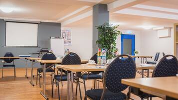 A conference room with tables, chairs, a projector screen, a whiteboard, and a blue door.