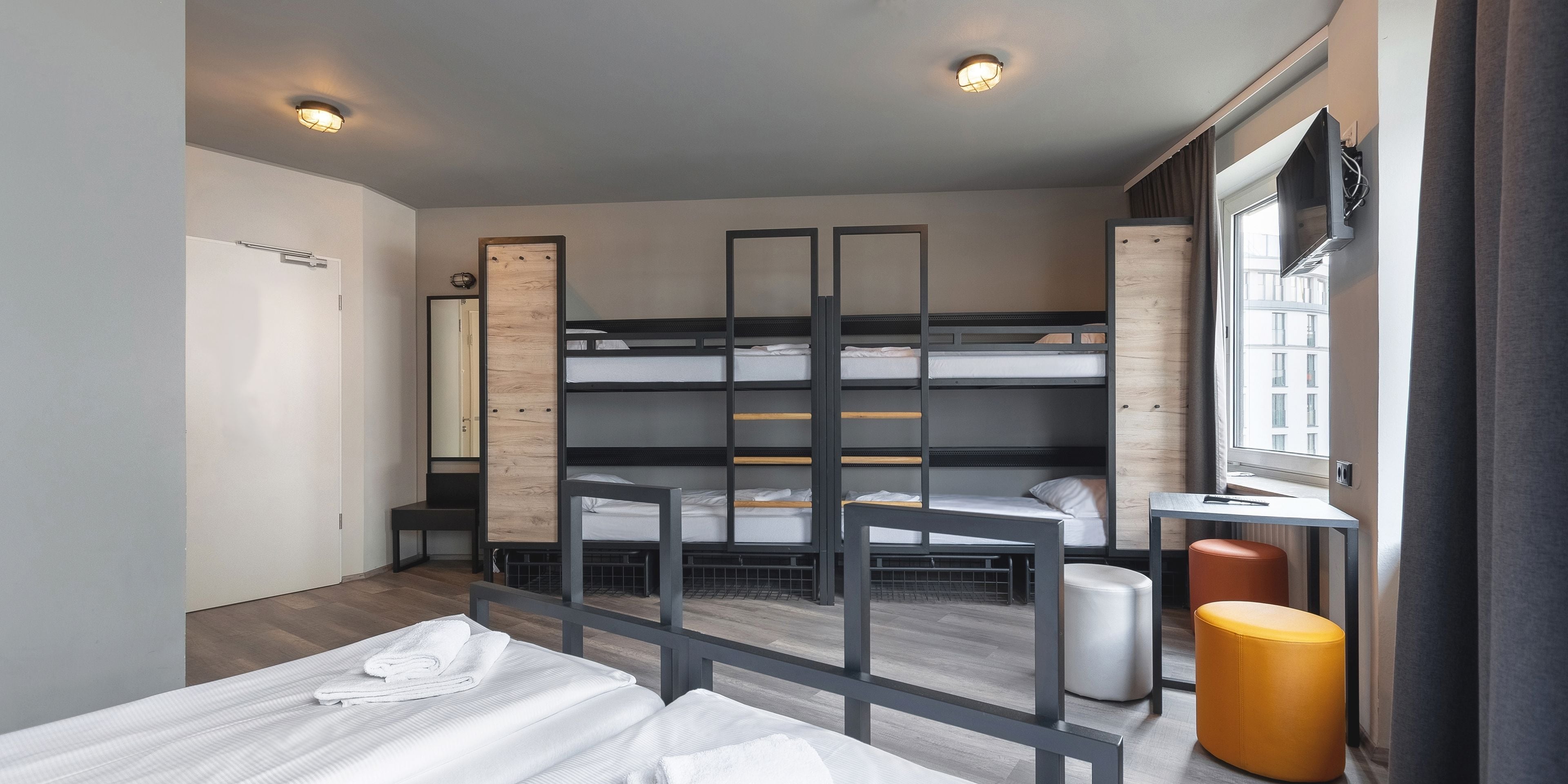 A modern hotel room with bunk beds, a desk, a chair, and a window with curtains.