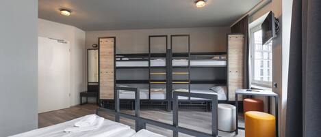 A modern hotel room with bunk beds, a desk, a chair, and a window with curtains.
