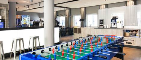 A modern indoor space with a foosball table, bar area, and seating.
