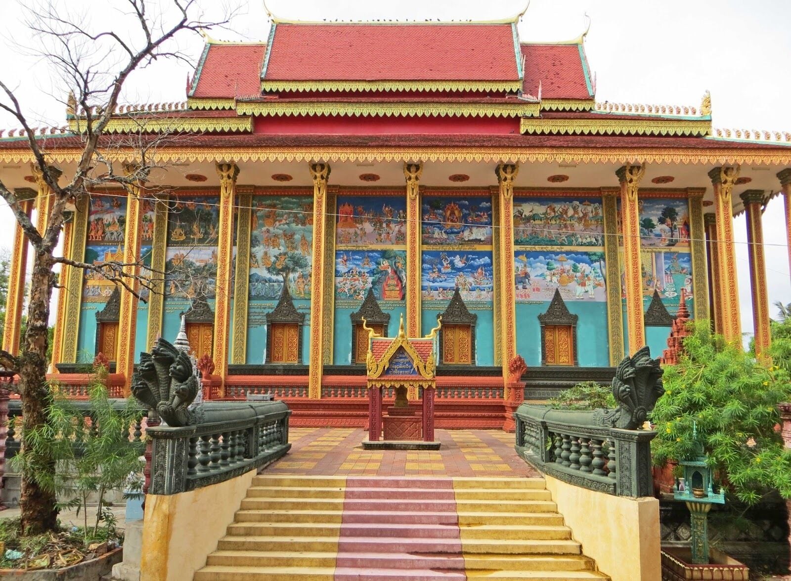 A traditional temple with a red roof, golden decorations, and a mural depicting various scenes.