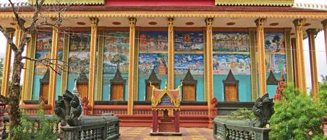 A traditional temple with a red roof, golden decorations, and a mural depicting various scenes.